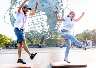Two tap dancers mid-air in front of Unisphere