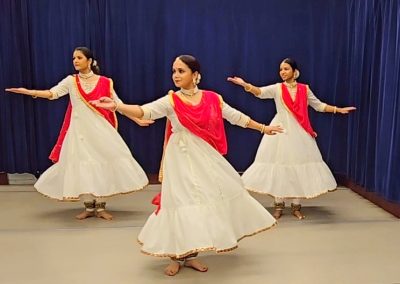 Trio of Kathak dancers in beige and red, arm reaching to side
