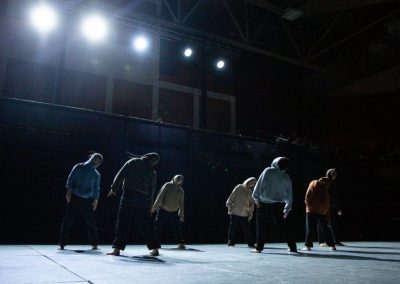 Group of dancers wearing hoodies leaning to right, shadowy lighting