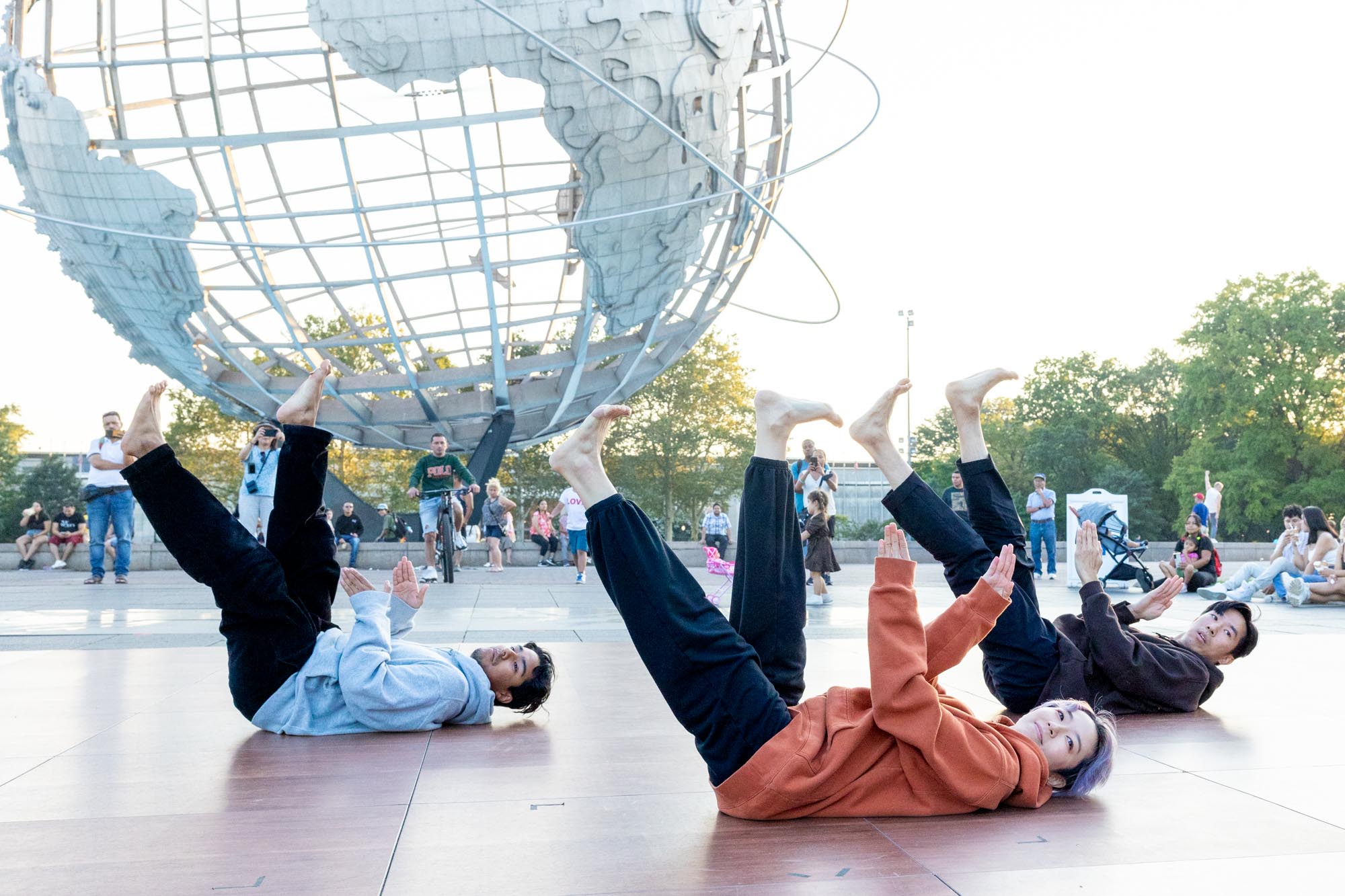 3 dancers on their back with feet and arms posed up, Unisphere in background