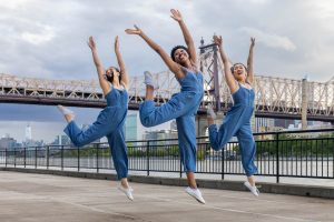 3 dancers wearing blue jumping in air, Queensborough Bridge in background